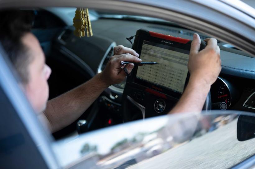 Technician reading a diagnostic scan tool from the driver's seat