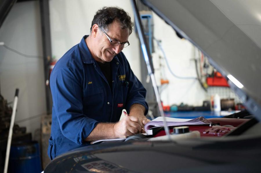 Mechanic writing up a job under a bonnet