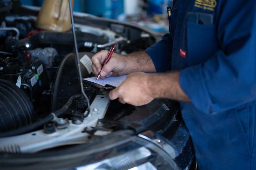 Mechanic filling in an inspection sheet over an engine bay